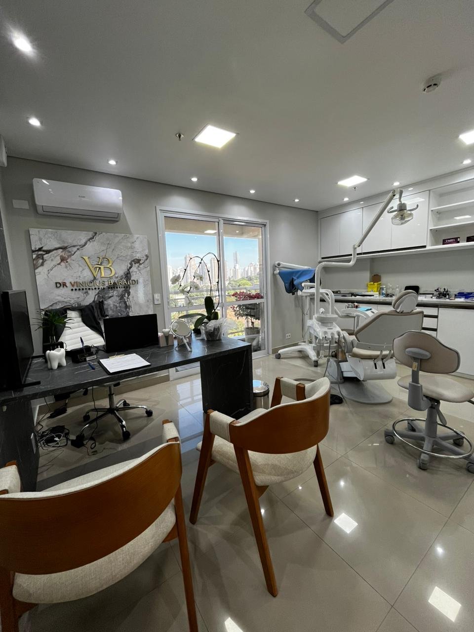 Consultório do Dr. Vinicius Baraldi com cadeira odontológica, mesa de atendimento e vista para São Paulo